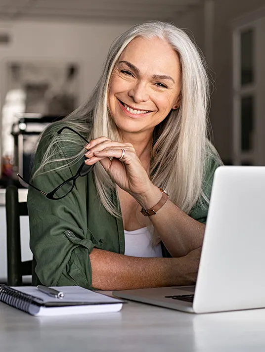Smiling woman sitting in front of a laptop and holding a pair of glasses