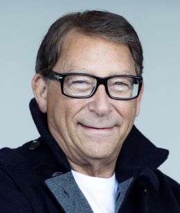 Headshot of Stuart Weitzman smiling, wearing black glasses and black jacket