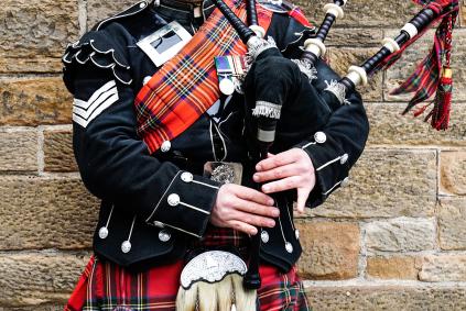 Scottish bagpiper dressed in traditional red and black tartan dress